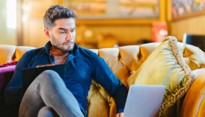 home de meia idade fazendo checkin no sofá de casa através de um notebook com Wi-fi