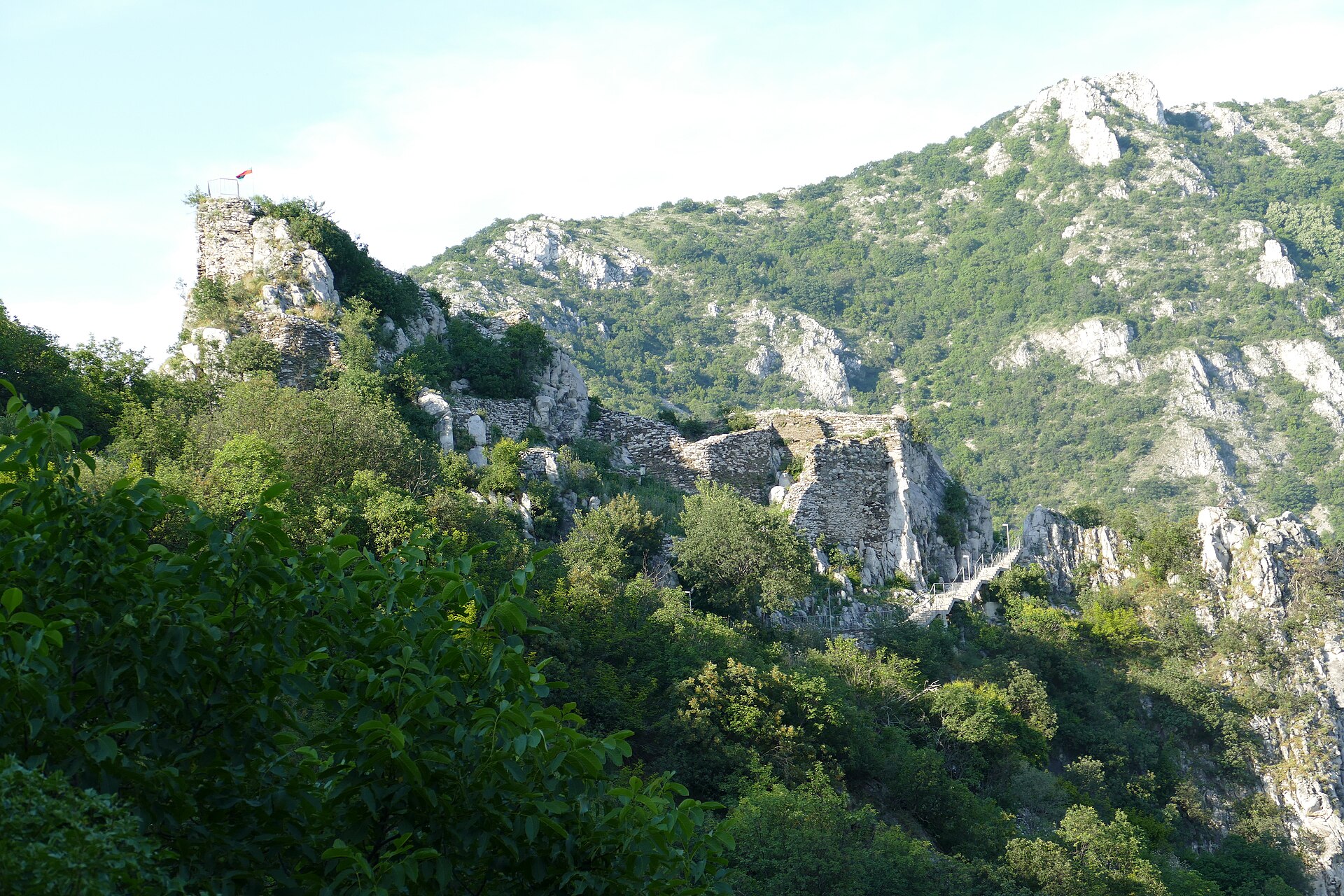 Ruínas de muralhas de pedra da Fortaleza de Asen no alto de um penhasco, cercadas por vegetação e montanhas