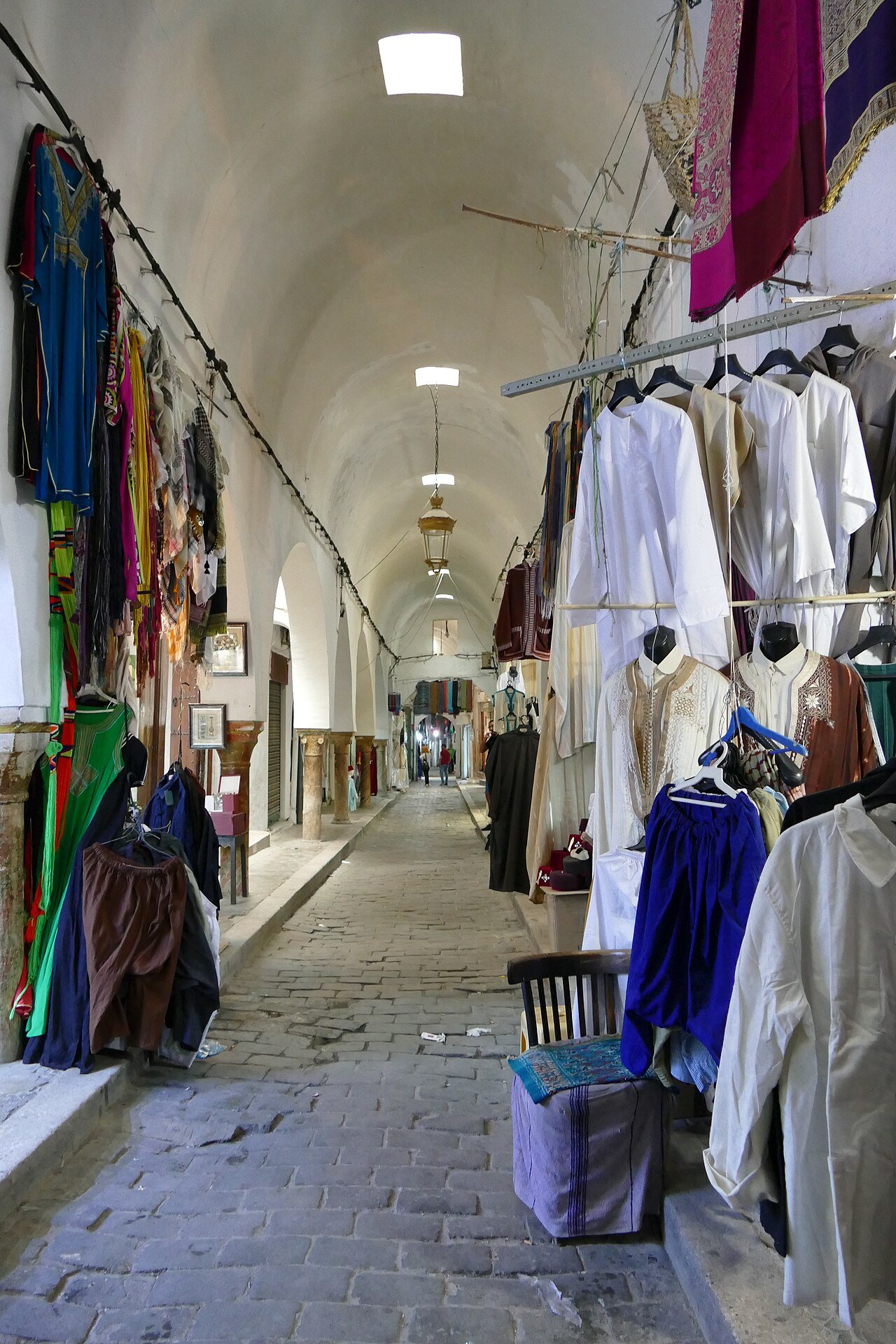 Viela coberta de um souk na medina de Tunes, com roupas e tecidos pendurados nas lojas