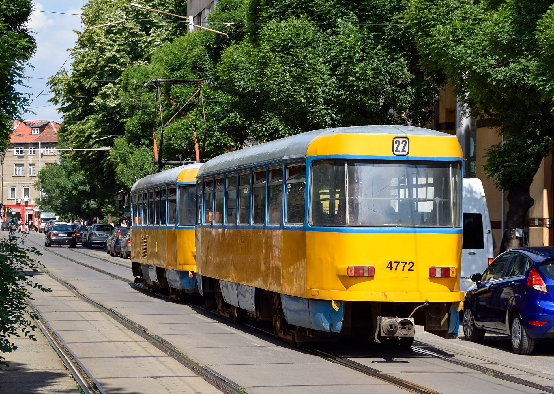 Bonde amarelo e azul de dois vagões, linha 22, circulando por uma rua arborizada de Sofia