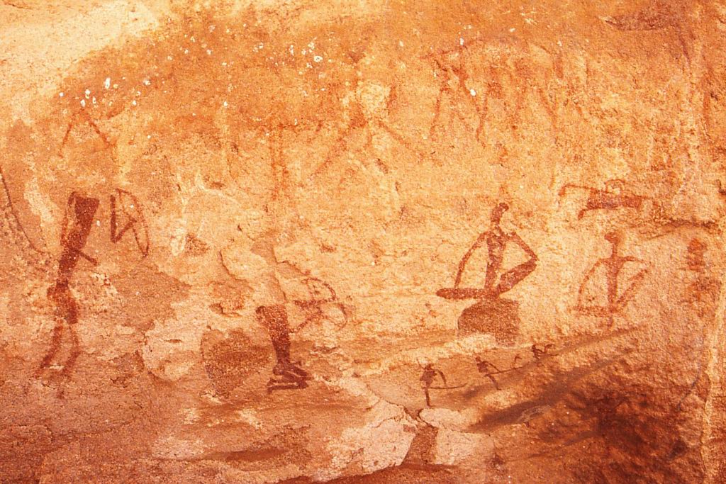 Figuras humanas esquemáticas pintadas em ocre e marrom sobre uma parede de rocha alaranjada