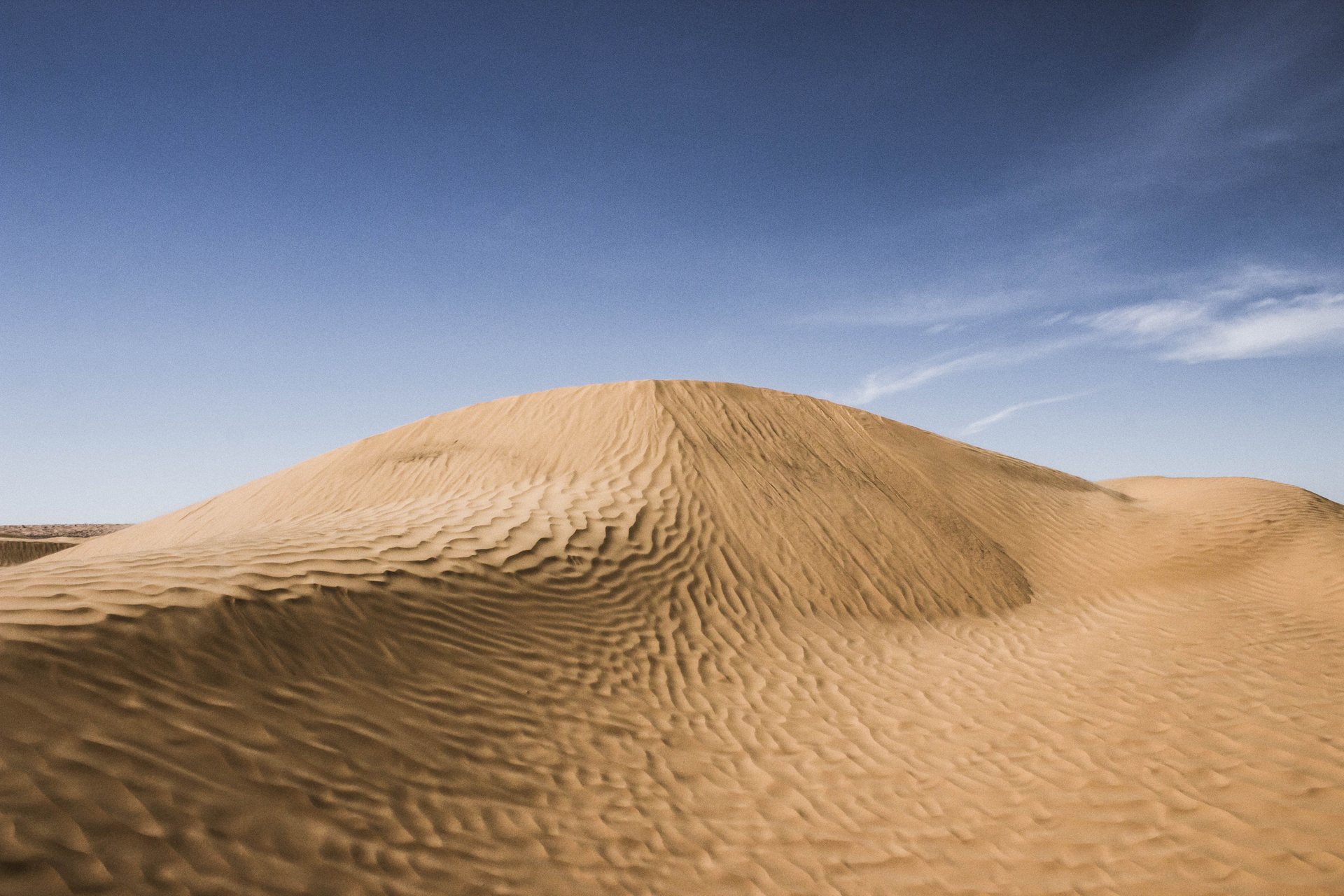 Duna de areia dourada com ondulações do vento em Ksar Ghilane